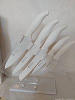 Six white-handled knives in clear acrylic stand