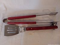 Metal BBQ tongs and spatula with wooden handles laid flat on white background.