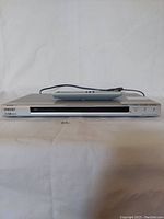 Front view of the silver Sony DVD/CD player model DVP-NS50P with remote cable on top, showing disc slot and control buttons.
