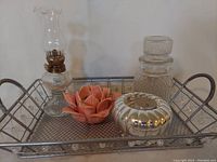 Full view of metal tray holding pink ceramic flower tealight holder, silver metal tealight holder, glass jar with lid, and oil lamp with chimney.