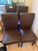 Four brown dining chairs grouped together, showing upholstery and legs.