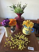 Top-down view of three vases each containing artificial floral stems in various colors and one laid flat yellow artificial floral stem on table.