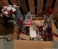 Overhead view of box with mixed red and silver Christmas decorations including flowers, pine cones, stars, berry sprigs, and bead garland