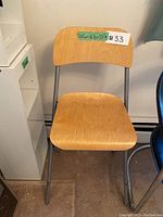 Chair with wooden seat and backrest, gray metal tubular legs, placed on a carpeted floor next to a white shelving unit.