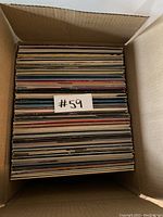 Cardboard box filled with many vinyl records viewed from above showing the top edges and thicknesses of the record sleeves.