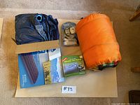 Camping gear including orange sleeping bag, boxed Escort twin air mattress, boxed Texsport electric air pump, and AM/FM radio in packaging