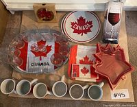 Full display of Canada Day themed party items including mugs, glasses, serving platters, napkins, and an accessory.