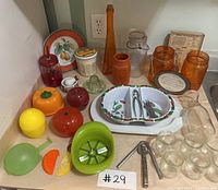 Photo shows a collection of colorful kitchen accessories, including mason jars, various plastic fruit peelers, a divided ceramic dish with fruit patterns, glass jars, and other utensils.