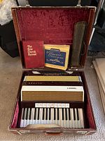 Accordion inside its open original case alongside two music books: 'The New Church Hymnal' and 'Keystone Music Notation Book'.