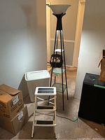 Full view of the tall lamp with glass shelves, step stool, and laundry basket in a hallway setting.