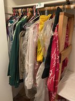 Photo of hanging men's clothing including shirts and jackets of varied colors and styles, some shielded in garment bags.