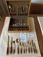 Photo of the entire 55-piece nickel bronze and rosewood cutlery set arranged in a wooden storage box and laid out on a table showing full contents and care instructions.