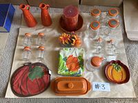 Full lot showing all kitchenware items including bottles, jars, candle, butter dish, napkins, and pot holders arranged on a beige surface with #3 marker.
