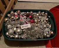 Wide view of green storage bin with assorted red and silver Christmas ornaments and silver tinsel inside.