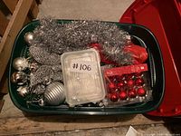 Photo showing green bin filled with silver and red Christmas decorations including tinsel, ornaments, and butterfly decoration