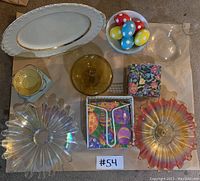 Top-down view of vintage glassware and Easter decorations on a brown surface including platter, glass bowls, Easter eggs, napkins, and a lantern.