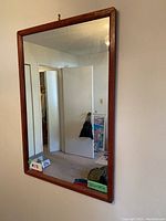 Front view of the rectangular wood framed wall mirror hanging on a white wall, showing the size and condition of the frame and mirror glass.