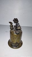 Front view of brass blowtorch showing valve knob, nozzle, and legible manufacturer mark embossed on the body with signs of heavy use and patina.