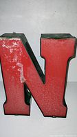 Front and left angled view of vintage red and green neon letter N sign from the 1950s showing wear and texture on surface.