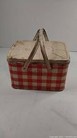 Front view of the 1950s tin picnic basket showing red and white checkered design and two metal handles on top.