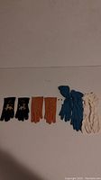 All six pairs of gloves laid out including black gloves with yellow poodle motif, tan, blue, and white gloves