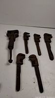 Six antique adjustable pipe wrenches of varying size laid out on a white surface showing heavy rust and wear