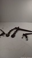 Three antique metal fence chain tighteners shown on a plain surface against a blank background, two larger with chain links and hooks, one smaller with two hooks.