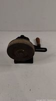 The antique hand cranked bench grinder with mounting bracket and wooden handle shown from the side on a white background.