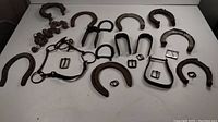 Overview of multiple rusty horseshoes, metal brackets, buckles, and horse tack components laid out on a white surface.