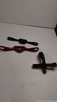 Three antique leather bookbinding tools laid out on a white surface including the pistol grip draw gauge, a red Stanley 51 spokeshave, and a black Record 63 spokeshave.