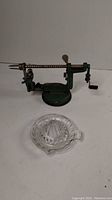 Metal apple peeler and glass citrus juicer on white surface.