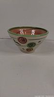 Side view of the conical handmade ceramic bowl showing colorful spiral designs and green rim.
