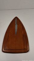 Top view of teak wooden cutting board with original cutter knife inserted, showing teak wood grain and knife handle