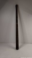 Full view of an antique wooden baseball bat with dark staining and Canadian markings