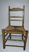 Front view of early antique wooden chair showing wooden frame and recaned seat