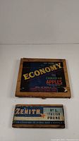 Two wooden fruit box crate end boards. Larger board labeled 'Economy Canadian Apples' with colorful vintage label. Smaller board labeled 'Zenith No. 1 Italian Prune' with blue and white vintage label.