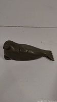 Side angled view of the dark soapstone seal carving, showing its smooth shape and flippers.