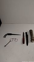 Photo showing all four items: lorgnette glasses without lenses, woodcutter tool with metal handle, Mora cutter with wooden handle, 1930s flashlight.