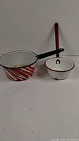 Photo showing both the painted enamel water ladle with striped pot and smaller white pot side by side