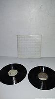Two vinyl records and original white dust jacket with brick wall pattern placed on a white surface.