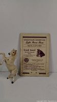Photo showing cream-colored rearing ceramic horse figurine next to the 1954 Saskatoon Exhibition Light Horse Show book.