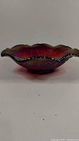 Side view of red carnival glass bowl showing scalloped edge and iridescent coloring.