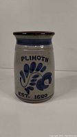 Front view of ceramic pottery crock featuring blue leaf pattern, 'PLIMOTH EST. 1620' text, and glazed brown rim.