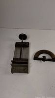 Swivel tabletop vise and wooden sad iron handle placed on white background; vise shows clamp base and screw handle for tightening.