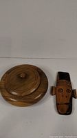 Photo of a round wooden teak bowl with lid next to a small carved tiki monkey figurine, shown on white background.