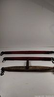 Three antique yokes, two long red painted with metal hooks, one natural wood with central metal bracket and hooks