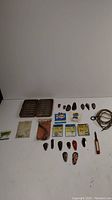 Overview photo showing assortment of vintage fishing tackle laid out on white surface including lures, sinkers, tackle boxes, fishing line, and other items.