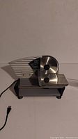 Front and side view showing slicer blade, food carriage, and base with attached power cord.