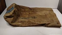 Tan canvas military duffle bag laid on white surface showing overall shape and condition.