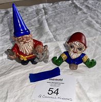 Front view of two ceramic gnome figurines on a white cloth background with auction lot number card visible.